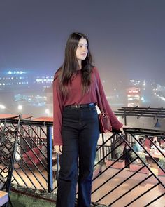 a woman standing on top of a balcony next to a railing with lights in the background