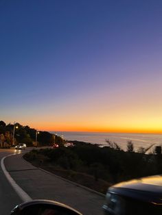 a car driving down the road at sunset with water in the background and trees to the side