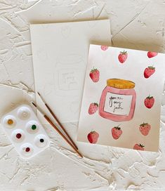 a card with strawberries and a jar of jam next to some paintbrushes