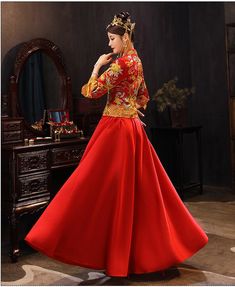 a woman in a red and gold dress standing next to a dresser with a mirror