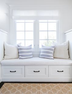 two pillows are sitting on a white bench in front of a window with windowsills