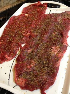 two raw steaks on a white plate with seasoning sprinkled over them