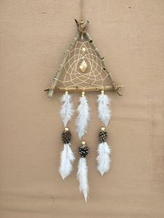 a white dream catcher hanging on a wall with feathers and pine cones attached to it