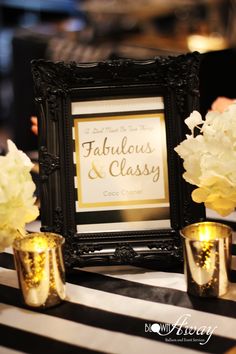 there are flowers and candles on the table in front of an old framed sign that says fabulous & classy