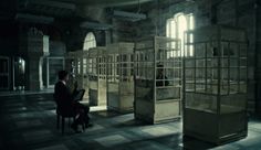 a man sitting at a desk in an empty room with lots of cages on the floor