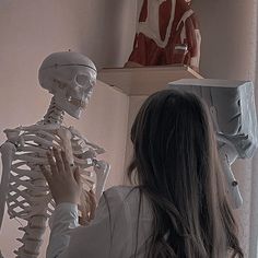 a woman looking at a skeleton in front of a man with a clock on the wall