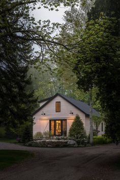 a white house surrounded by trees in the evening with its lights on and windows lit up