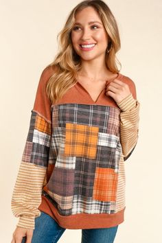 a woman wearing an orange and brown sweater with plaid print on the sleeves, standing in front of a white background