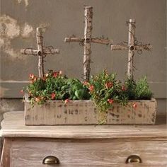 a wooden box with flowers in it on a table next to a cross and wall