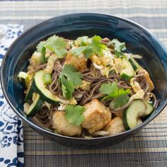 a bowl filled with noodles and vegetables on top of a blue table cloth next to a fork