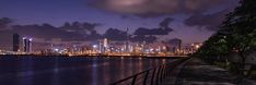 the city skyline is lit up at night with clouds in the sky and reflecting on the water