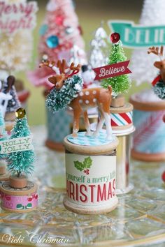 miniature christmas trees and reindeer figurines are on a glass table with tinsel