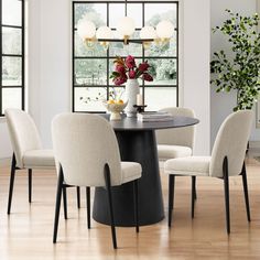 a dining room table with four chairs and a vase filled with flowers on it in front of a large window