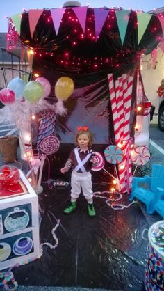 a doll is standing in front of a tent with balloons and streamers on it