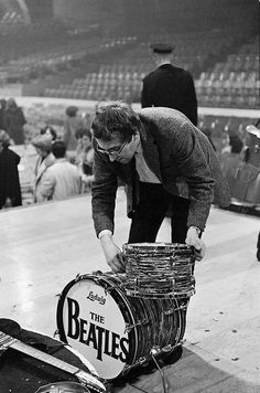 an old photo of a man leaning over a drum case with the beatles logo on it