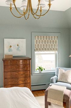 a bedroom with blue walls and white bedding, a chandelier and a chair