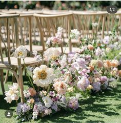 rows of wooden chairs lined up with flowers in them on the grass at an outdoor ceremony