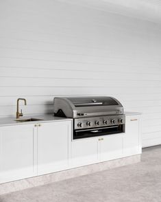 an outdoor kitchen with white cabinetry and stainless steel counter tops, along with a gold faucet