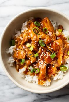 a white bowl filled with chicken and rice on top of a marble countertop next to chopsticks