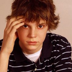 a young boy sitting at a table with his hand on his head and looking off to the side