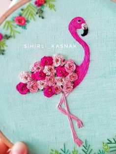 a pink flamingo with flowers in it's beak is embroidered onto a light blue hoop