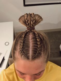 a woman with two braids in her hair looking down at the ground while wearing a yellow shirt