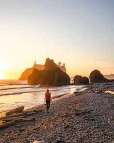 a woman walking on the beach at sunset with rocks in the background and water behind her