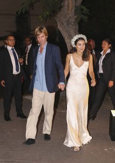 a man and woman holding hands walking down the street with other people in the background