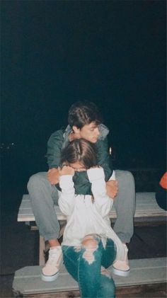 two people sitting on a bench with one person covering his face and the other holding him