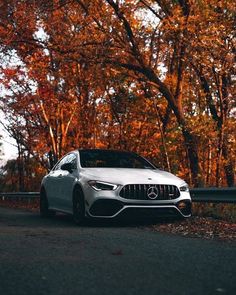 a white car parked on the side of a road in front of trees with orange leaves