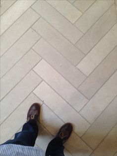 a person standing on the floor in front of a white brick wall and wearing brown shoes