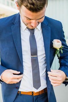 a man in a blue suit and tie is looking down at his pocket while holding a flower