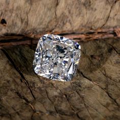 a cushion cut diamond sitting on top of a piece of wood with bark behind it