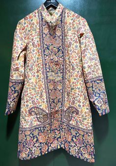 Step into elegance with our Woven Wool Kani Jamawar Coat, adorned with an intricate paisley floral pattern on both the front and back. This soft and lightweight trench coat is an ideal choice for spring and cool summer days, providing both style and comfort. Crafted from the renowned Kashmiri Kani shawl, woven with traditional techniques in Kashmir, this coat is a beautiful and timeless piece. The same Kani Shawl fabric is expertly tailored into this coat, ensuring a seamless blend of heritage and contemporary fashion. The coat's interior is lined with soft, silky, color-coordinated fabric, featuring convenient side pockets and a discreet hook enclosure on the front. With a vibrant play of colors, this jacket is a graceful addition to any occasion, effortlessly enhancing your casual and tr Fitted Nehru Jacket With Floral Print And Long Sleeves, Fitted Long Sleeve Nehru Jacket With Floral Print, Festive Long Sleeve Outerwear With Floral Print, Festive Floral Print Long Sleeve Outerwear, Festive Long Sleeve Floral Print Outerwear, Traditional Nehru Jacket With Floral Print, Festive Fitted Outerwear With Floral Print, Fitted Floral Print Outerwear For Festive Season, Bohemian Long Sleeve Floral Print Outerwear