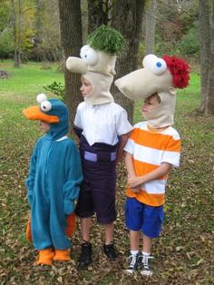 three children in costume standing next to each other near trees and grass with heads on their heads