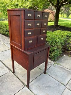 an old wooden dresser sitting on the side of a sidewalk next to some bushes and trees