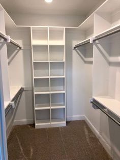 an empty walk in closet with white shelving and brown carpeting on the floor