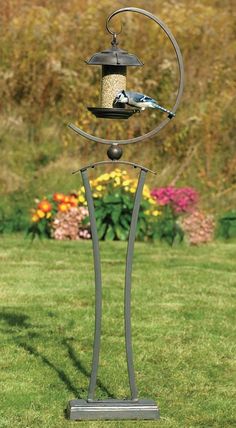 a bird feeder on top of a metal pole in the middle of some grass and flowers