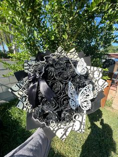 a black and white bouquet with butterflies on it in front of a tree, next to the grass