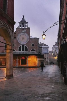 a clock tower in the middle of a city street at dusk with people walking around