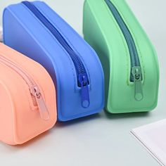 three different colored zippered bags sitting on top of a white table next to each other