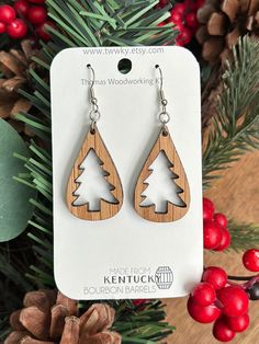 wooden earrings with trees on them sitting next to pine cones and evergreen needles in front of a christmas tree