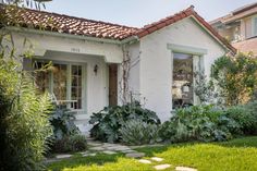 a white house with green plants in front of it and a stone path leading to the door