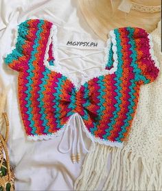 a crocheted top with fringes and a straw hat on the bed next to it