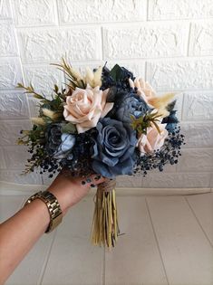 a hand holding a bouquet of blue and pink flowers in front of a white brick wall