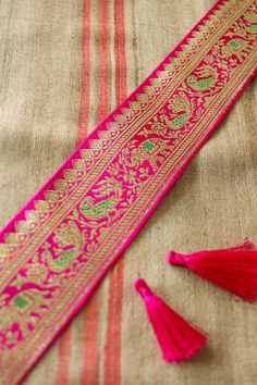 pink and gold tassels are laying on top of a striped table cloth,