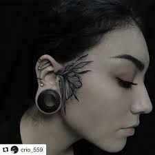 a woman wearing ear piercings with an artistic design on her face and behind her ear