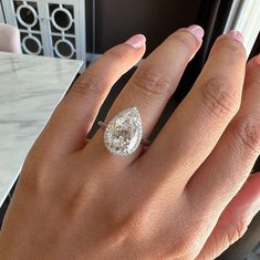 a woman's hand with a diamond ring on top of her finger, near a window