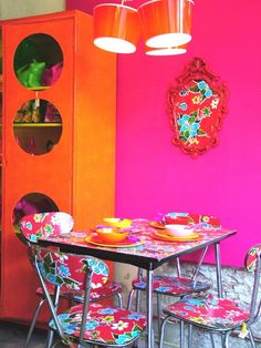 a dining room table with colorful chairs and a red cabinet in the backround