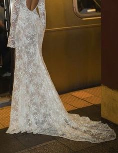 a woman standing in front of a train with her back to the camera, wearing a long sleeved wedding dress